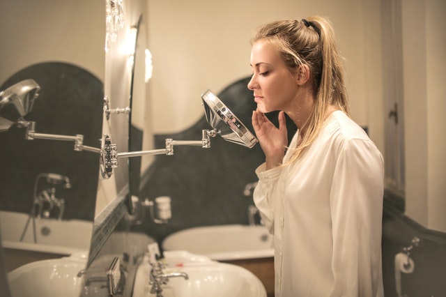 Self-checking your skin A young woman uses a small mirror in her bathroom to check her skin